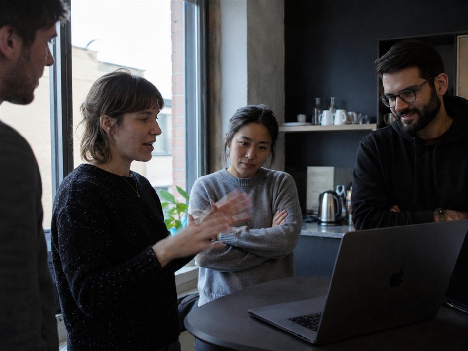 Four colleagues gathered around a laptop while a teammate explains her approach